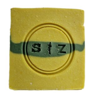 Vierkante zeepbar van voren gezien, geel van kleur met een groene streep in het midden. In het midden van de zeep is een rond logo gestempeld met de tekst 's & z'.