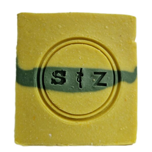 Vierkante zeepbar van voren gezien, geel van kleur met een groene streep in het midden. In het midden van de zeep is een rond logo gestempeld met de tekst 's & z'.